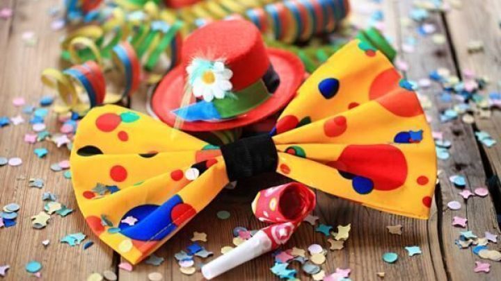 Eine bunte Krawatte liegt auf einem Holztisch, umgeben von Konfetti und kreisf&ouml;rmigen Luftschlangen, passend zum Karneval.