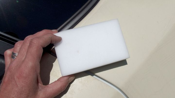 Ein Schmutzradierer wird in der Hand gehalten, w&auml;hrend damit schwarze Flecken von einer autolackierten Oberfl&auml;che entfernt werden.