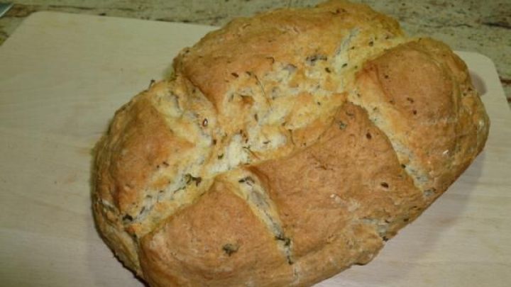 Ein frisch gebackenes Buttermilchbrot liegt auf einem Holzbrett in einer K&uuml;che und weist eine goldbraune Kruste auf.