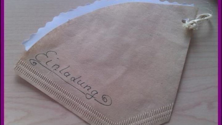 Eine selbstgemachte Einladungskarte aus braunem Papier, beschriftet mit "Einladung", liegt auf einem Tisch. Schlichtes Design.
