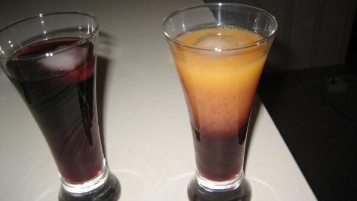 Zwei Gl&auml;ser mit bunten Getr&auml;nken stehen auf einem Tisch, eines in tiefem Rot und das andere in strahlendem Gelb-Orange.