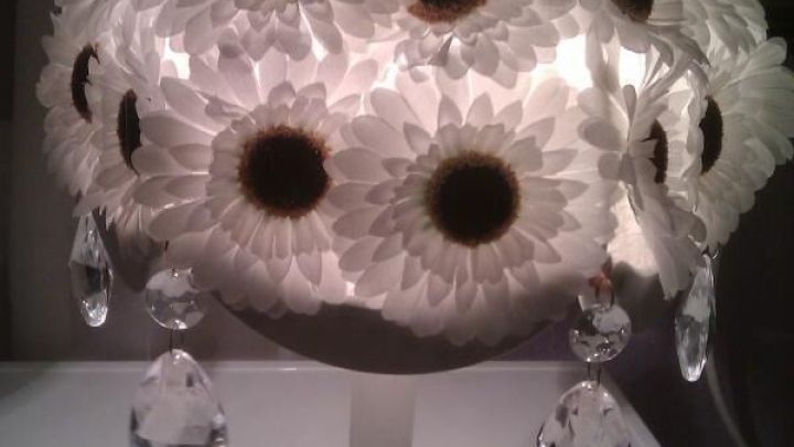 Eine Schreibtischlampe mit einem Lampenschirm aus Sonnenblumen, die im weichen Licht des Raums strahlt und glitzert.