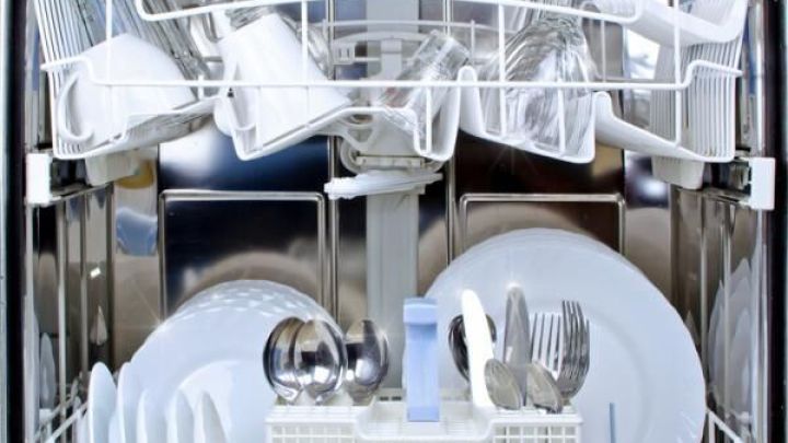 Die Sp&uuml;lmaschine w&auml;scht Geschirr und Besteck; innen gl&auml;nzend sauber, gef&uuml;llt mit Tellern, Gl&auml;sern und Tassen.