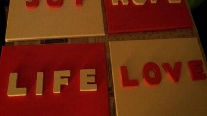 Bunte Leinw&auml;nde zeigen Worte wie "JOY", "HOPE", "LIFE" und "LOVE" auf wei&szlig;em und rotem Hintergrund in kreativer Wanddeko.