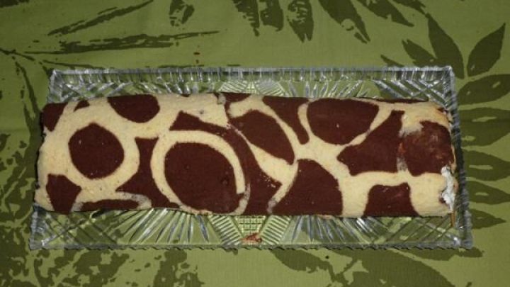 Eine gemusterte Biskuitrolle liegt auf einer gr&uuml;nen Unterlage und zeigt ein lebhaftes Giraffenmuster aus Teig.