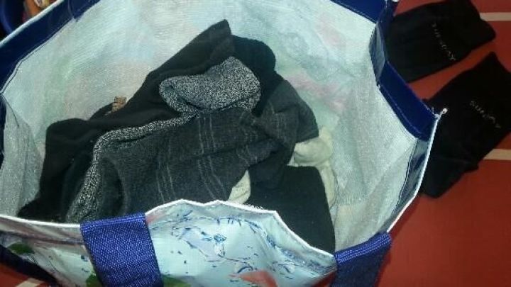Eine Einkaufstasche enth&auml;lt mehrere Socken, steht auf einem Tisch neben weiteren, ordentlich gefalteten Sockenpaaren.