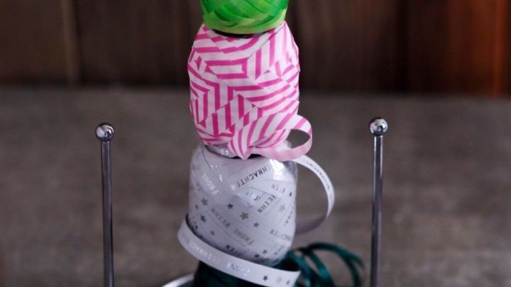 Ein Halter pr&auml;sentiert buntes Deko- und Organzab&auml;nder, ordentlich gestapelt, auf einer stabilen Metallbasis.