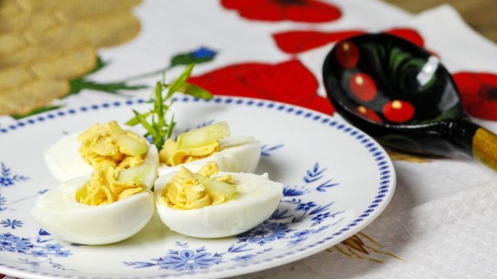 Auf einem Teller liegen russische Eier, die geh&auml;lft sind. Sie sind mit einer gelben F&uuml;llung dekoriert. Daneben ist ein sch&ouml;ner L&ouml;ffel.