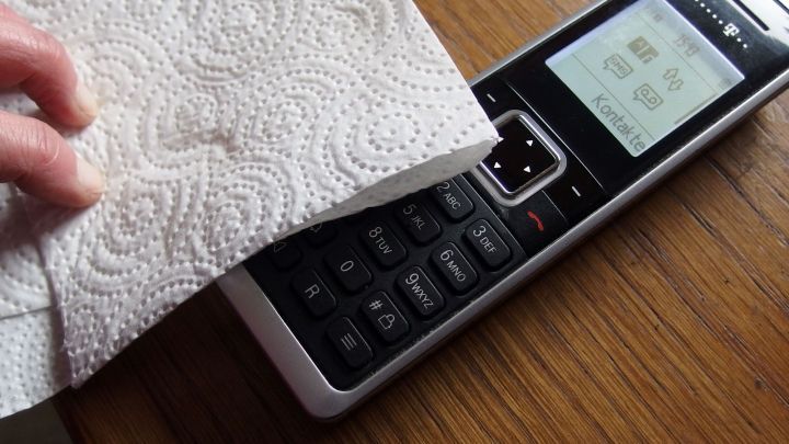 Ein Handtuch wischt einen Telefonh&ouml;rer ab, um die Hygiene am Arbeitsplatz zu gew&auml;hrleisten, auf einem Holztisch.