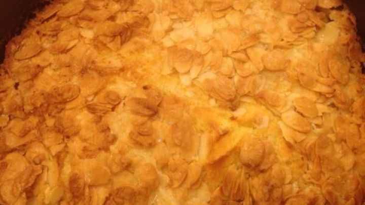 Ein goldbrauner Butterkuchen mit Mandeln liegt in einer runden Backform und wartet darauf, serviert zu werden.