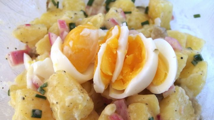 Ein Kartoffelsalat ist in einer Sch&uuml;ssel mit gew&uuml;rfelten Eiern und Schinken, bereit zum Servieren.
