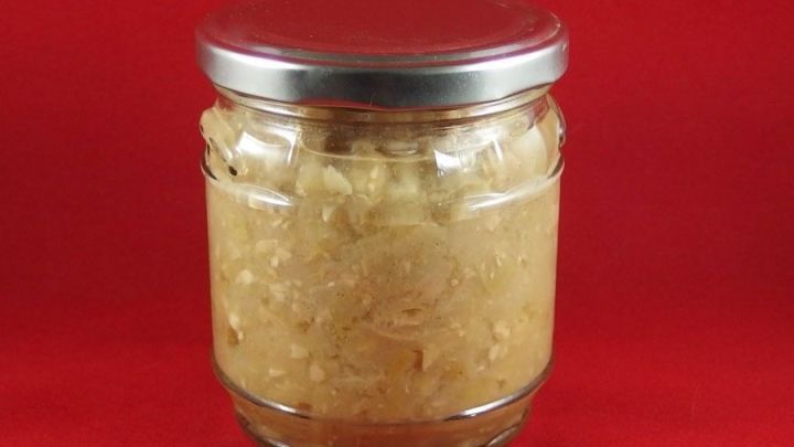 Ein Glas Apfelkompott steht vor rotem Hintergrund und zeigt die cremige, goldene Masse im Inneren des gl&auml;sernen Beh&auml;lters.