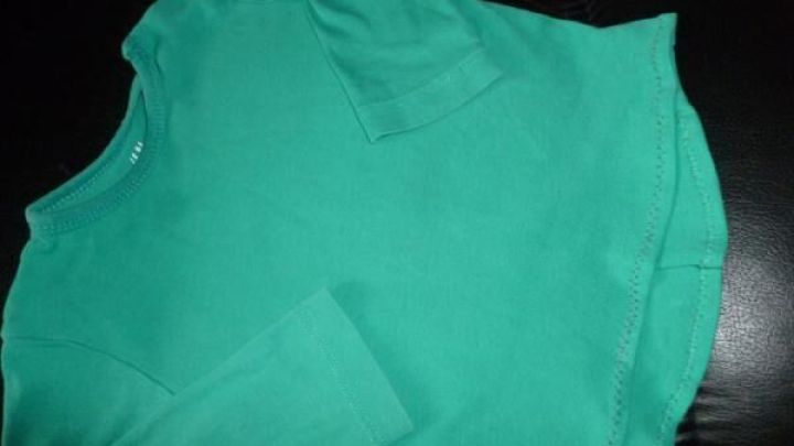 Ein gr&uuml;nes T-Shirt liegt auf einem schwarzen Lederstuhl. Es hat lange &Auml;rmel und sieht wie umgearbeitet aus.