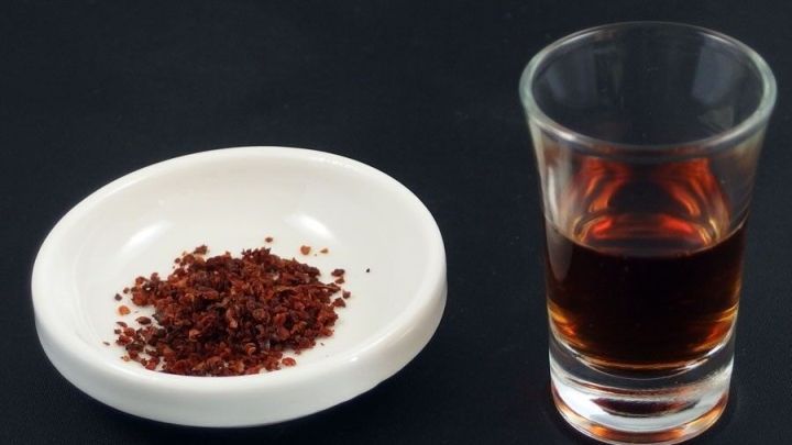 Rotem Pfeffer auf einem wei&szlig;en Teller neben einem Glas Essig, das als Hilfe gegen scharfes Essen dient.