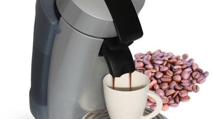 Eine silberne Senseo-Maschine br&uuml;ht Kaffee in eine Tasse, w&auml;hrend Kaffeebohnen daneben liegen, um das Kaffee-Setup zu vervollst&auml;ndigen.