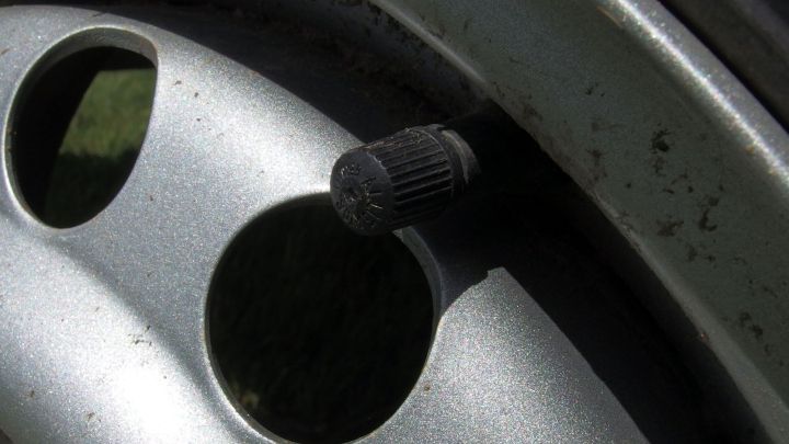 Eine Ventilkappe am Reifen wird gel&ouml;st, um den Luftdruck im Auto zu &uuml;berpr&uuml;fen, umgeben von einer Felge.