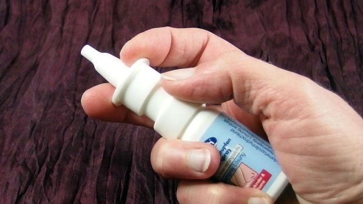 Ein Nasenspray wird von einer Hand gehalten, w&auml;hrend es auf einem dunklen Hintergrund vorbereitet wird, um das Ohrenknacken im Flugzeug zu lindern.