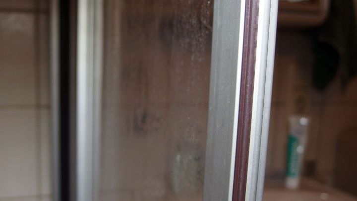 Eine Duschwand mit hartn&auml;ckigen Kalkflecken steht im Fokus, umgeben von einem Badezimmer mit weiteren Hygieneprodukten.