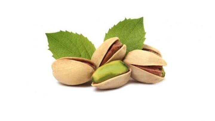 Pistazien liegen ge&ouml;ffnet auf einem wei&szlig;en Hintergrund, begleitet von gr&uuml;nen Bl&auml;ttern.
