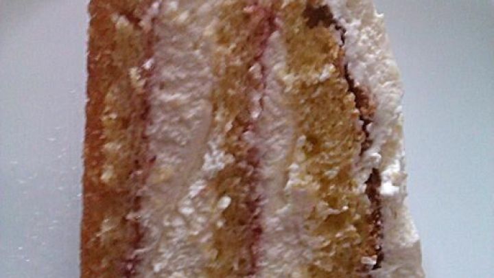 Eine Fr&uuml;hlingstorte auf einem Teller zeigt mehrere Schichten aus heller, luftiger Masse und cremiger F&uuml;llung.