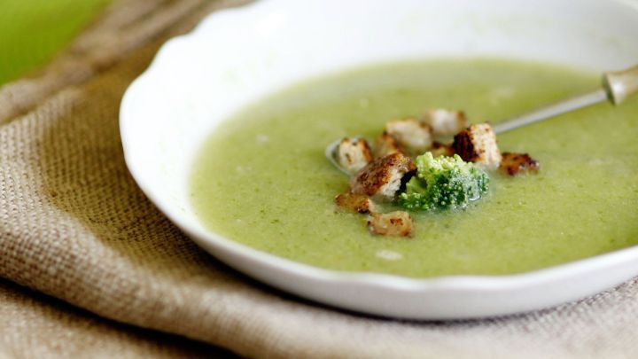 Brokkoli-Apfelcremesuppe in wei&szlig;em Teller auf grobem Stoff, garniert mit Croutons und Brokkoli.
