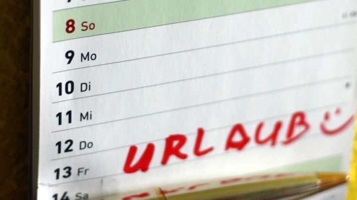 Ein Kalenderblatt zeigt den Sonntag, den 8. mit dem vermerkten Wort "URLAUB" in roter Schrift, daneben liegt ein Stift.