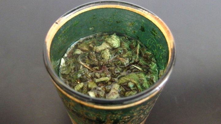 Ein Glas mit Salbeitee steht auf einem Tisch, der klare Inhalt zeigt Kr&auml;uter f&uuml;r freie Atemwege.