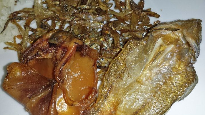 Gegrillter Fisch und knusprige Beilagen liegen auf einem wei&szlig;en Teller, umgeben von einer herzhaften &Ouml;lmarinade.