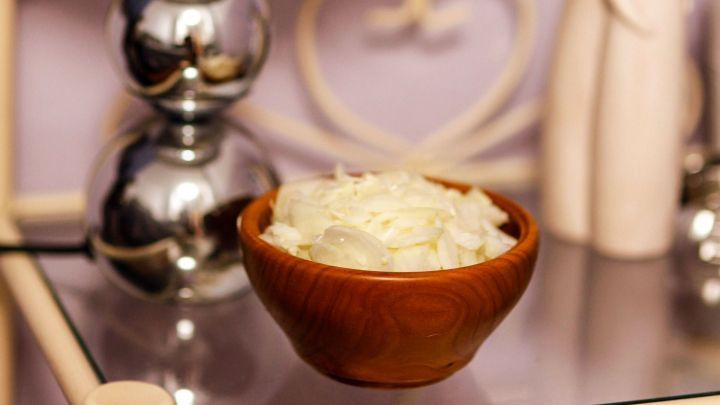 Eine Holtsch&uuml;ssel mit einer wei&szlig;en Substanz steht auf einem Tisch neben einer Lampe, die in einem gem&uuml;tlichen Raum leuchtet.