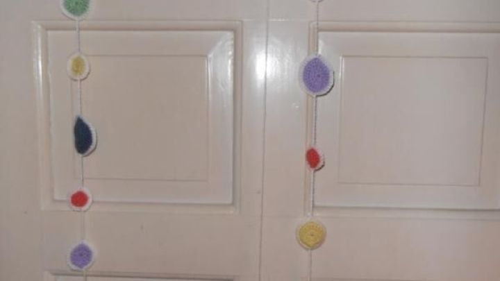 H&auml;kelketten h&auml;ngen vor wei&szlig;er T&uuml;r, zeigen bunte Kreise in Pastellfarben, wirken als verspielter Fadenvorhang.