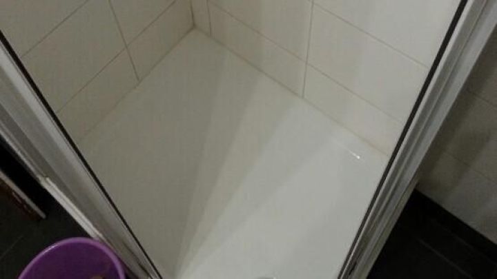 Eine saubere Dusche mit einem Abfluss in der Mitte und einem Eimer nebenan, bereit f&uuml;r die Dusche reinigen.