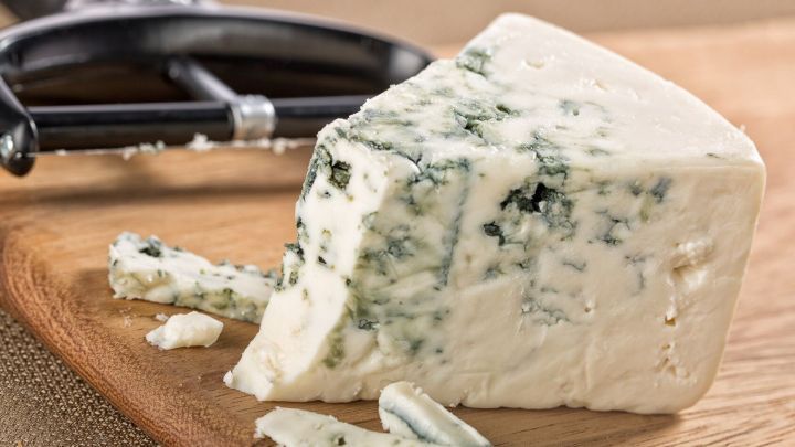 Ein St&uuml;ck Gorgonzola liegt auf einem Holzbrett neben einem K&auml;sehobel.