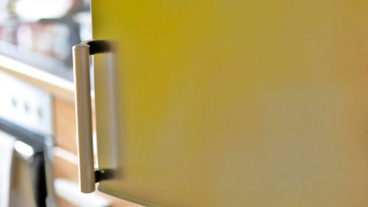 Ein Edelstahlgriff einer K&uuml;hlschrankt&uuml;r in einer K&uuml;che. Im Hintergrund ist ein Backofen zu erkennen.