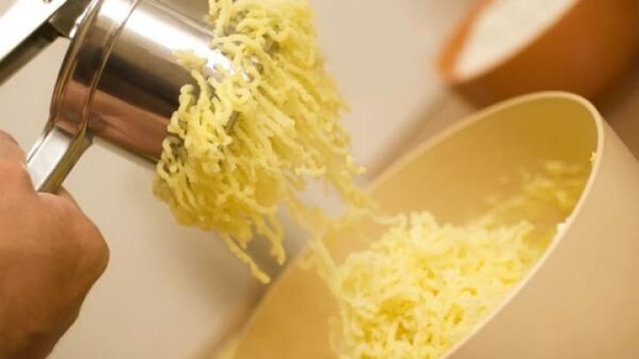 Eine Hand dr&uuml;ckt eine Kartoffelpresse, wodurch Kartoffeln in eine gro&szlig;e Sch&uuml;ssel gepresst werden.