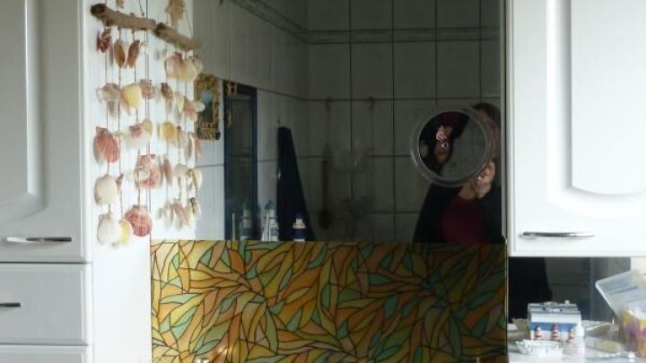 Ein Spritzschutz am Badezimmerspiegel sch&uuml;tzt die Wand vor Wasserspritzern w&auml;hrend der Benutzung des Waschbeckens in einem hellen, gefliesten Raum.