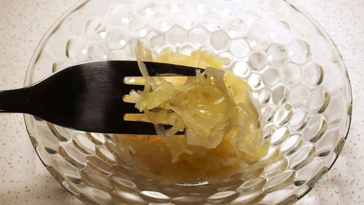 Eine Gabel hebt sauer eingelegtes Kraut aus einer dekorativen, transparenten Sch&uuml;ssel in einer hellen Umgebung.