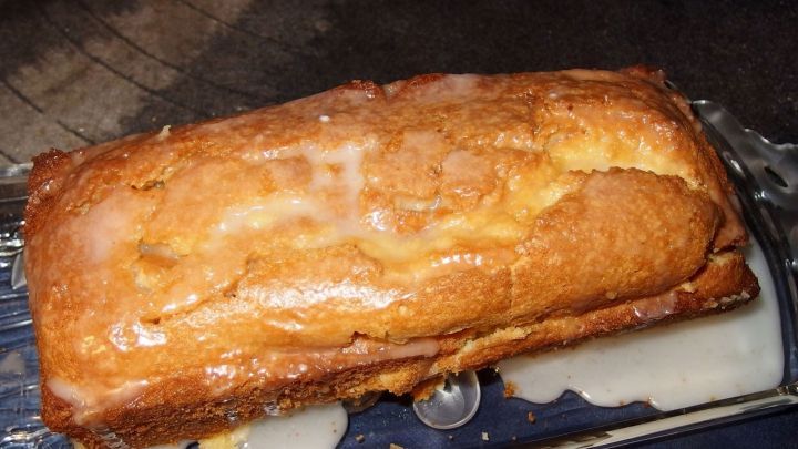 Ein Zitronenkuchen glasiert auf einer Glasplatte, umgeben von einem dunklen Untergrund.