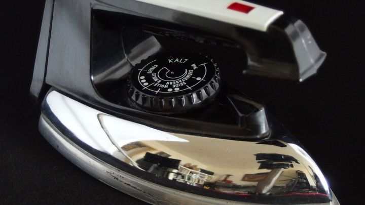 Ein B&uuml;geleisen liegt auf einem schwarzen Untergrund. Es gleitet &uuml;ber Stoff, um Falten zu entfernen und zu gl&auml;tten.