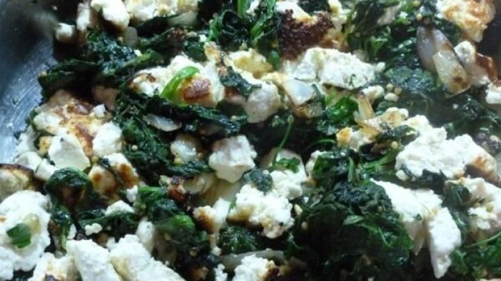 In einer Pfanne liegt eine Mischung aus frischem Spinat und selbstgemachtem Milchk&auml;se, die gebraten wird und dampft.