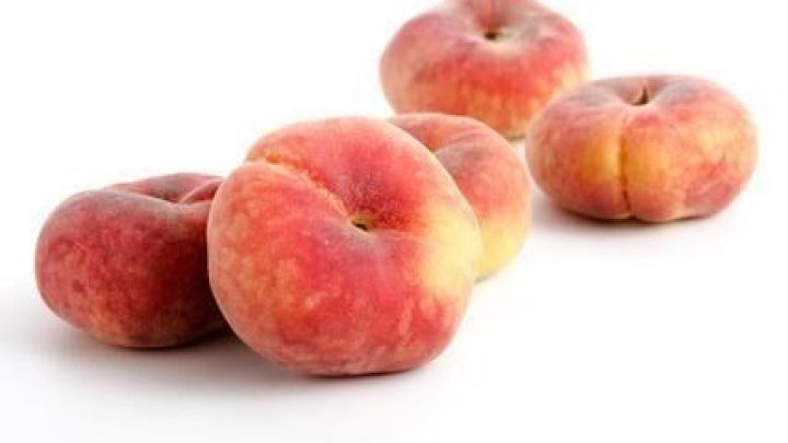 Mehrere flache Bergpfirsiche liegen verstreut auf einer wei&szlig;en Oberfl&auml;che. Sie zeigen ihre r&ouml;tlich-gelbe Haut.