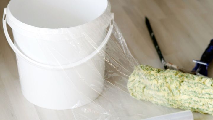 Ein Farbeimer, mit Folie ausgelegt, steht auf einem Tisch. Ein Farbroller liegt daneben, bereit f&uuml;r den Einsatz beim Streichen.