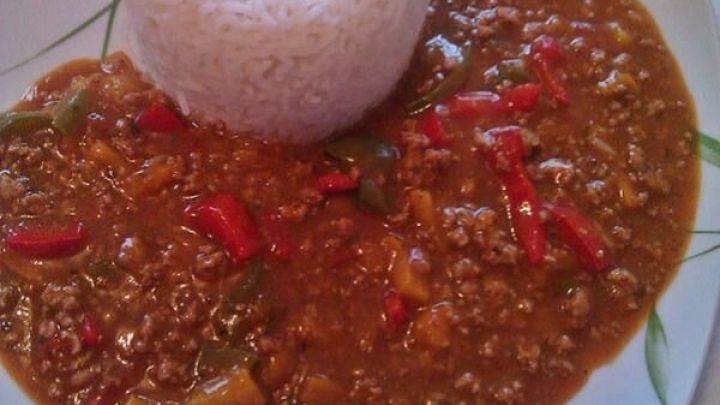 Eine bunte Paprika Pfanne liegt zusammen mit einem fluffigen Reis auf einem wei&szlig;en Teller. Die Paprika ist in einer w&uuml;rzigen Sauce angerichtet.