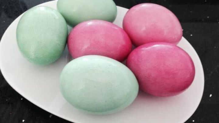 Bunte Ostereier liegen auf einem wei&szlig;en Teller, gef&auml;rbt mit Lebensmittelfarben in rosa und gr&uuml;n, auf dunklem Hintergrund.