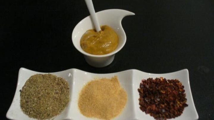 Senf in einem wei&szlig;en Gef&auml;&szlig; mit L&ouml;ffel, daneben Gew&uuml;rze in F&auml;chern auf dunklem, minimalistischem Hintergrund.