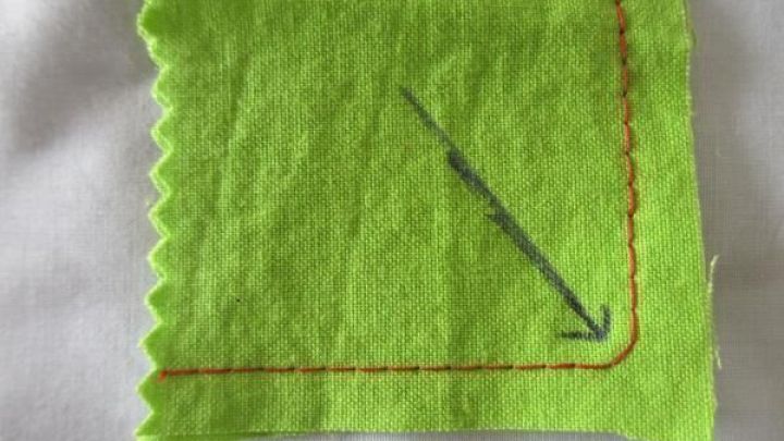 Gr&uuml;ner Stoff mit gen&auml;hter roter Ecke und Pfeil, der das Ausformen im Schneiderei-Kontext anzeigt.