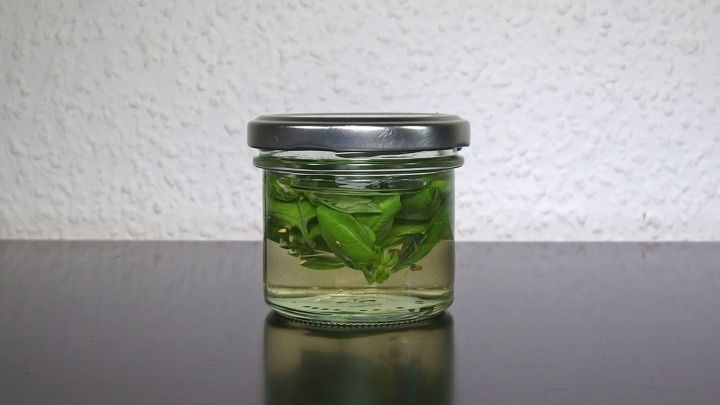Ein Glas mit Basilikumbl&auml;ttern in &Ouml;l steht auf einem dunklen Untergrund, um das Basilikum aufzubewahren.