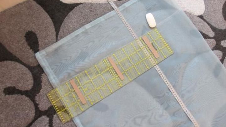 Ein transparenter Gardinenschal liegt flach auf einem gemusterten Teppich, w&auml;hrend ein Lineal zum Messen daneben positioniert ist.