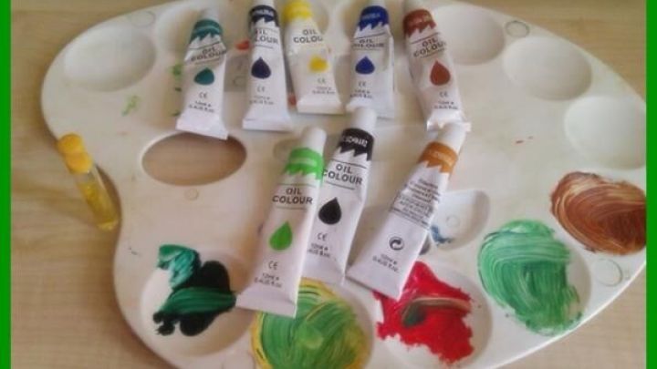 &Ouml;lfarbtuben liegen auf einer Farbmischpalette, einige Farben sind bereits gemischt. Der Tisch bietet einen neutralen Hintergrund.