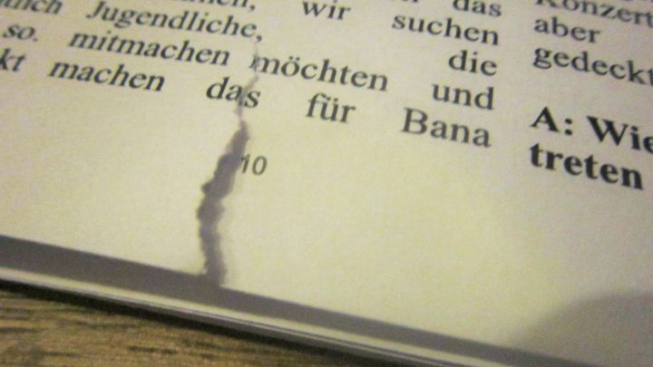 Eine eingerissene Buchseite liegt auf einem Holztisch, w&auml;hrend der Riss die Lesbarkeit beeintr&auml;chtigt.