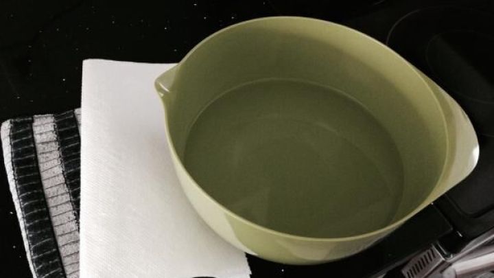 Eine gr&uuml;ne Sch&uuml;ssel mit Wasser steht neben einem Reinigungstuch auf einer K&uuml;chenoberfl&auml;che, bereit f&uuml;r klebrige Kocharbeiten.